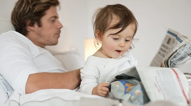 baby and father reading newspaper in bed in the morning