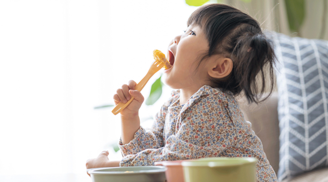 1 year old girl eating food with a fork