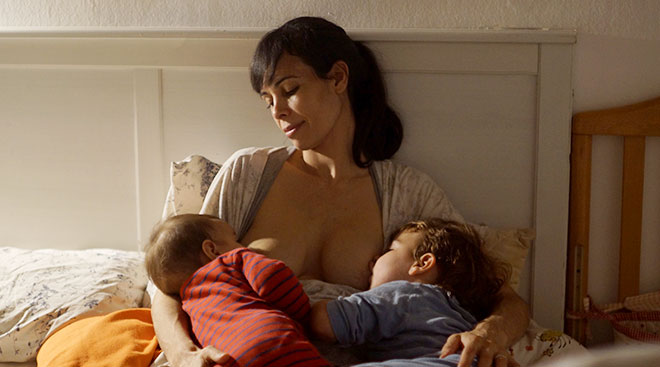 mother sitting in bed and tandem breastfeeding her two children
