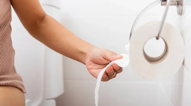 woman sitting on toilet and grabbing toilet paper
