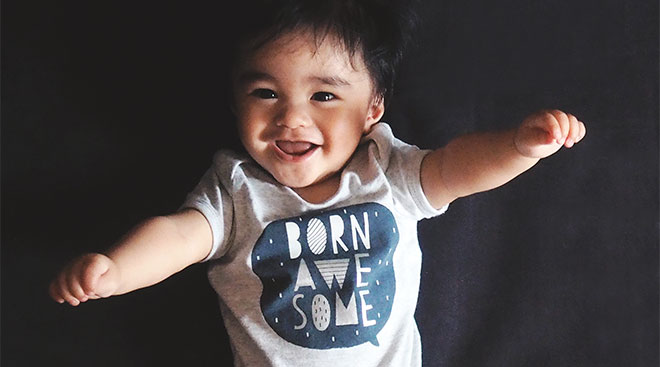 Happy baby wearing a onesie thats "born awesome."