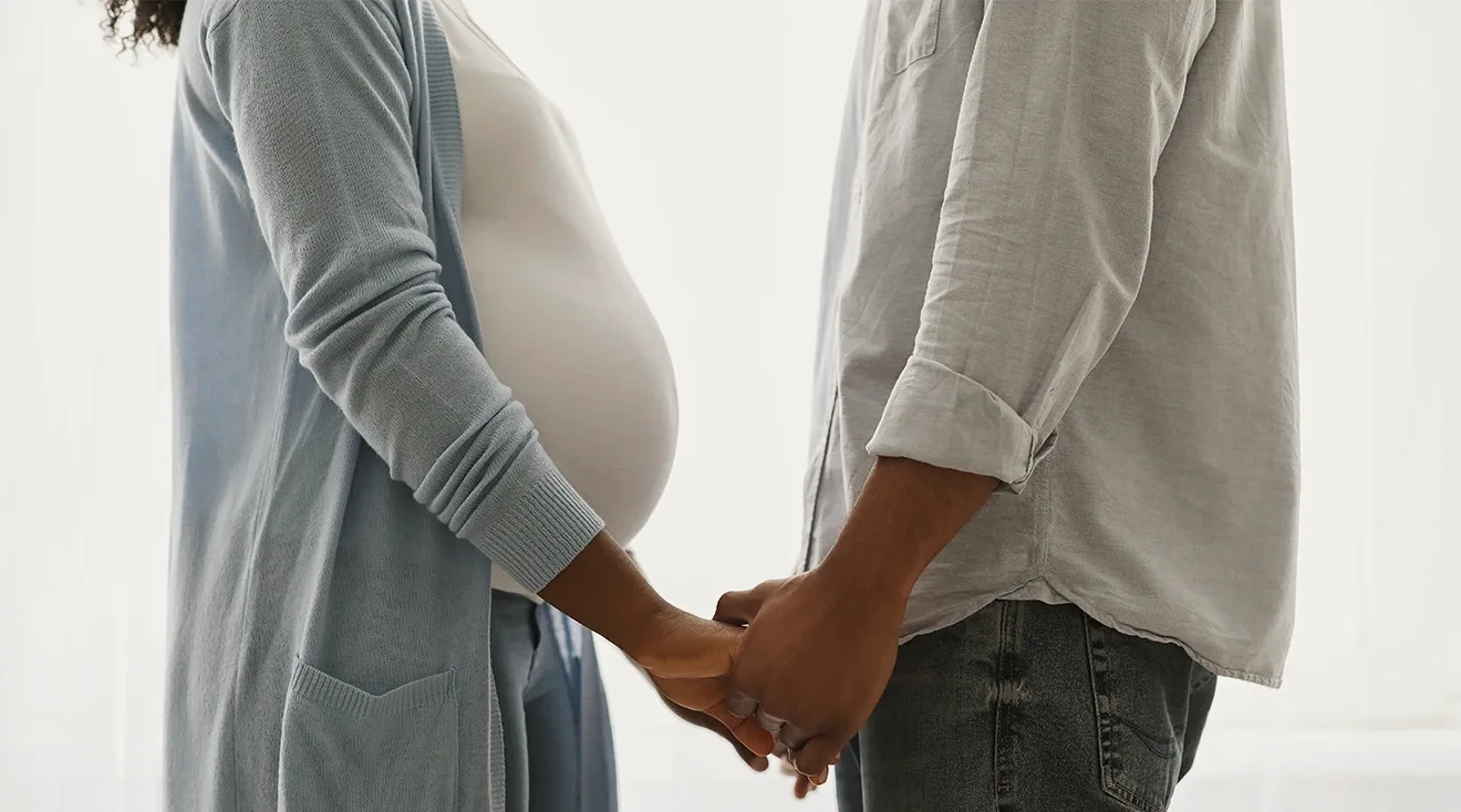 Pregnant woman and her husband stand opposite each other holding hands