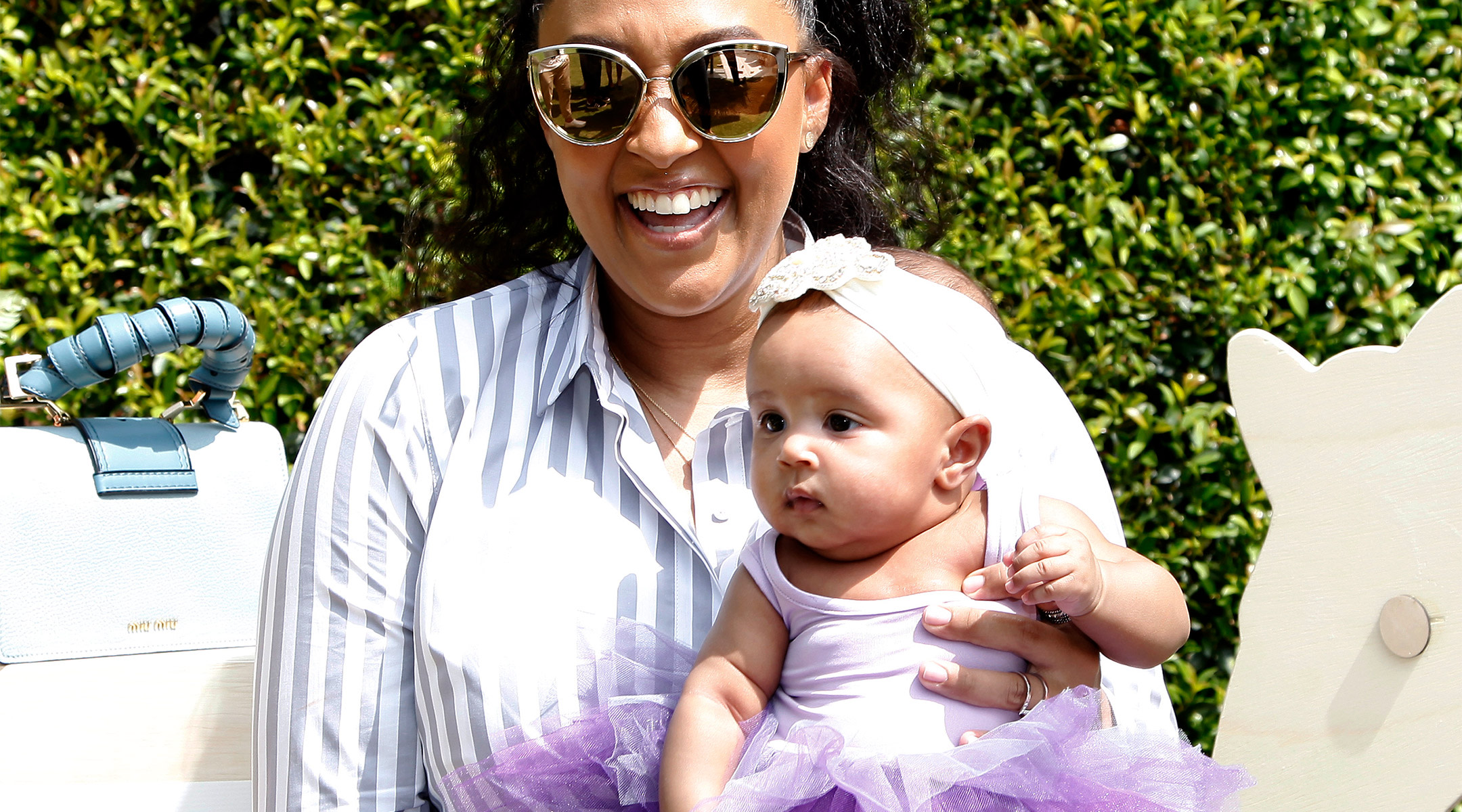 celebrity tia mowry happily holding her baby girl who is wearing a purple tutu