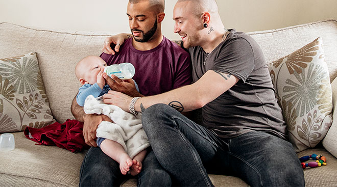 two happy dads feeding their baby at home