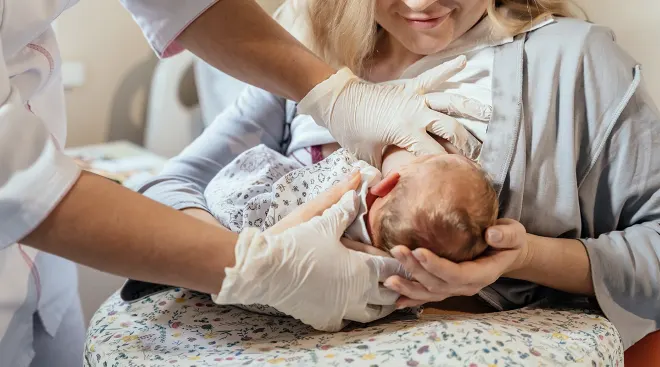 mother learning how to breastfeed newborn baby with nurse