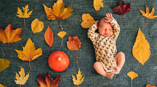 newborn baby photographed with fall leaves and a pumpkin