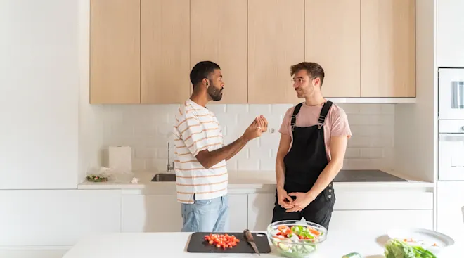 LGBTQ couple talking in the kitchen of their home while making dinner