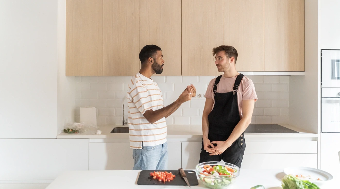 LGBTQ couple talking in the kitchen of their home while making dinner