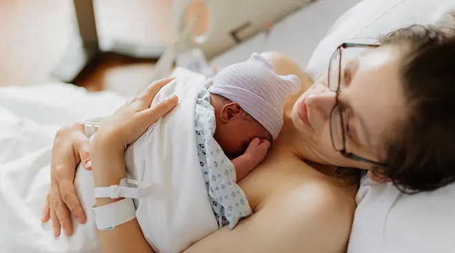 mother holding newborn baby in hospital bed