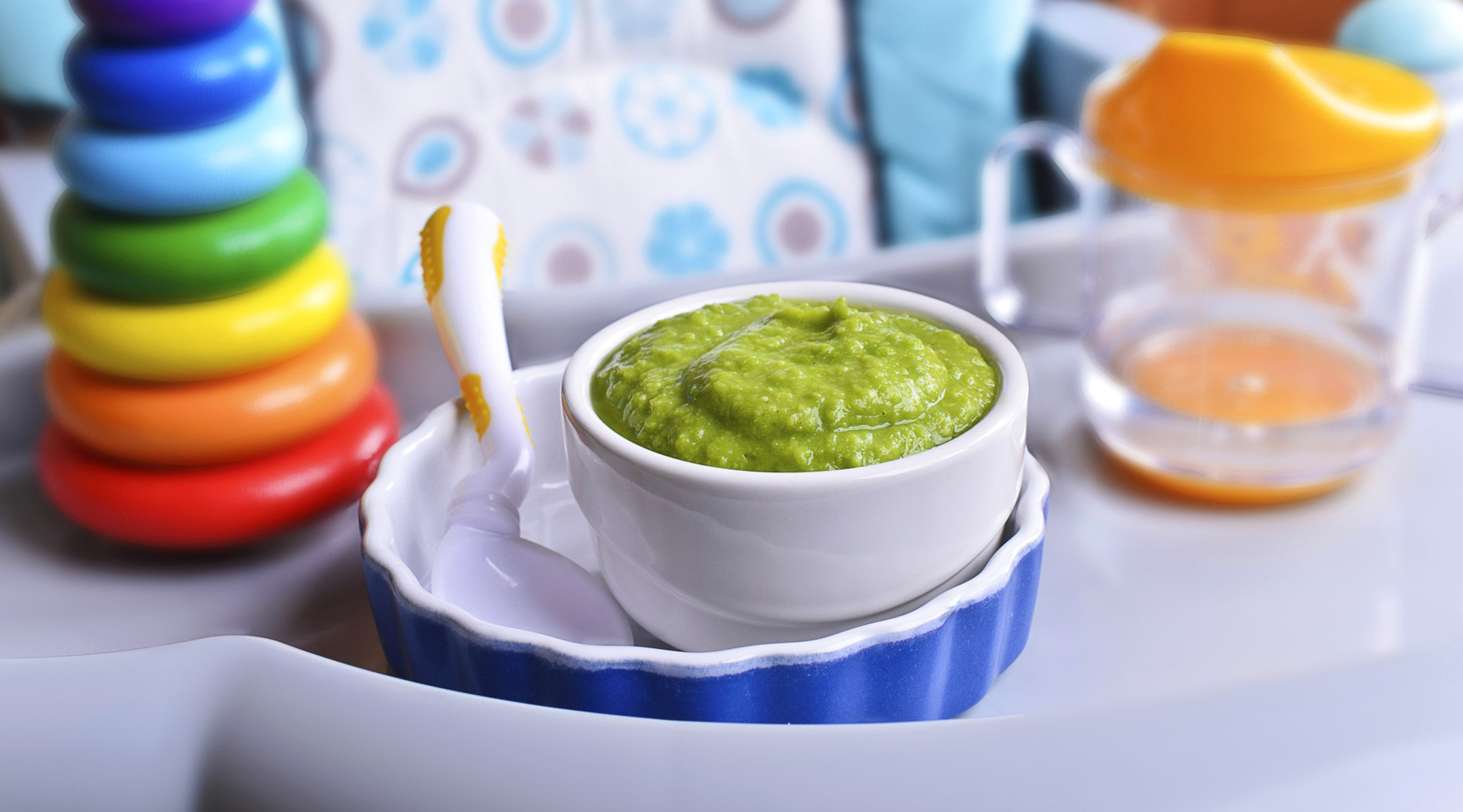 Detail of green baby food in bowl on high chair. 
