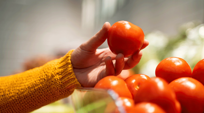 close up of hand holding a tomato inside grocery store