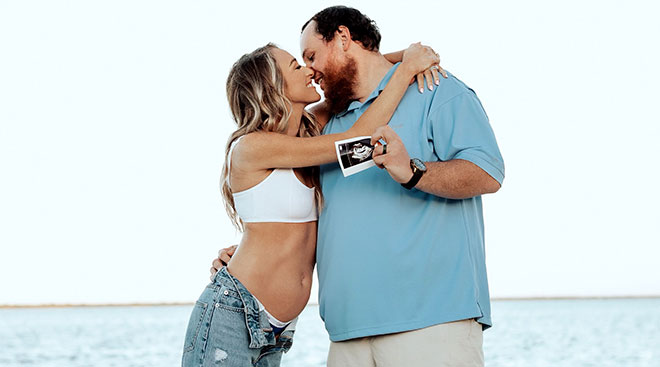Nicole and Luke Combs kissing on the beach while showing ultrasound for pregnancy annnoucement