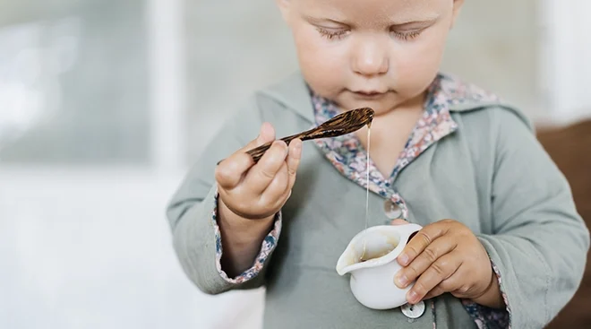 baby holding a jar of honey and a wooden spoon