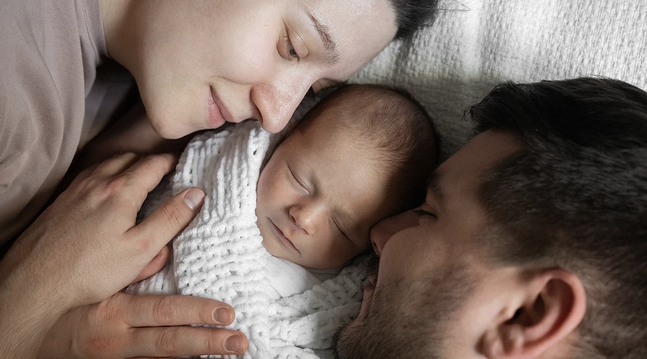 parents cuddling newborn baby at home