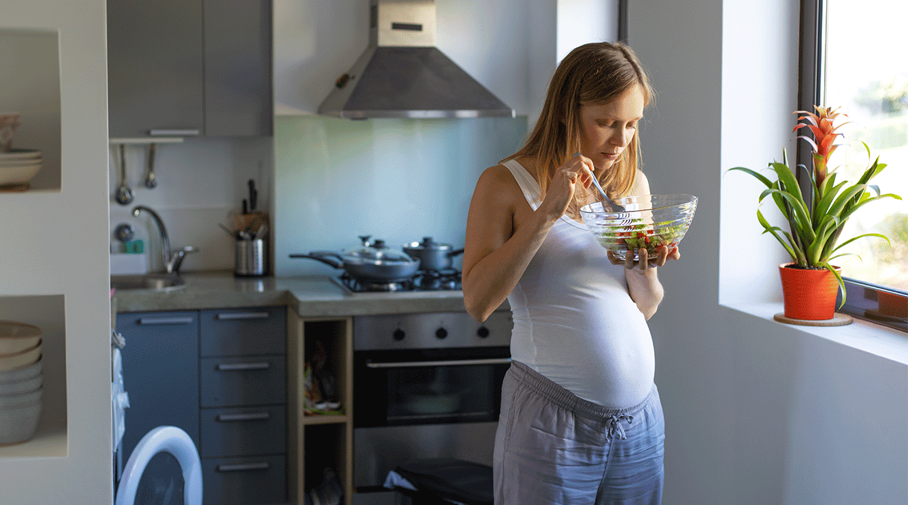 pregnant woman eating a salad in kitchen at home