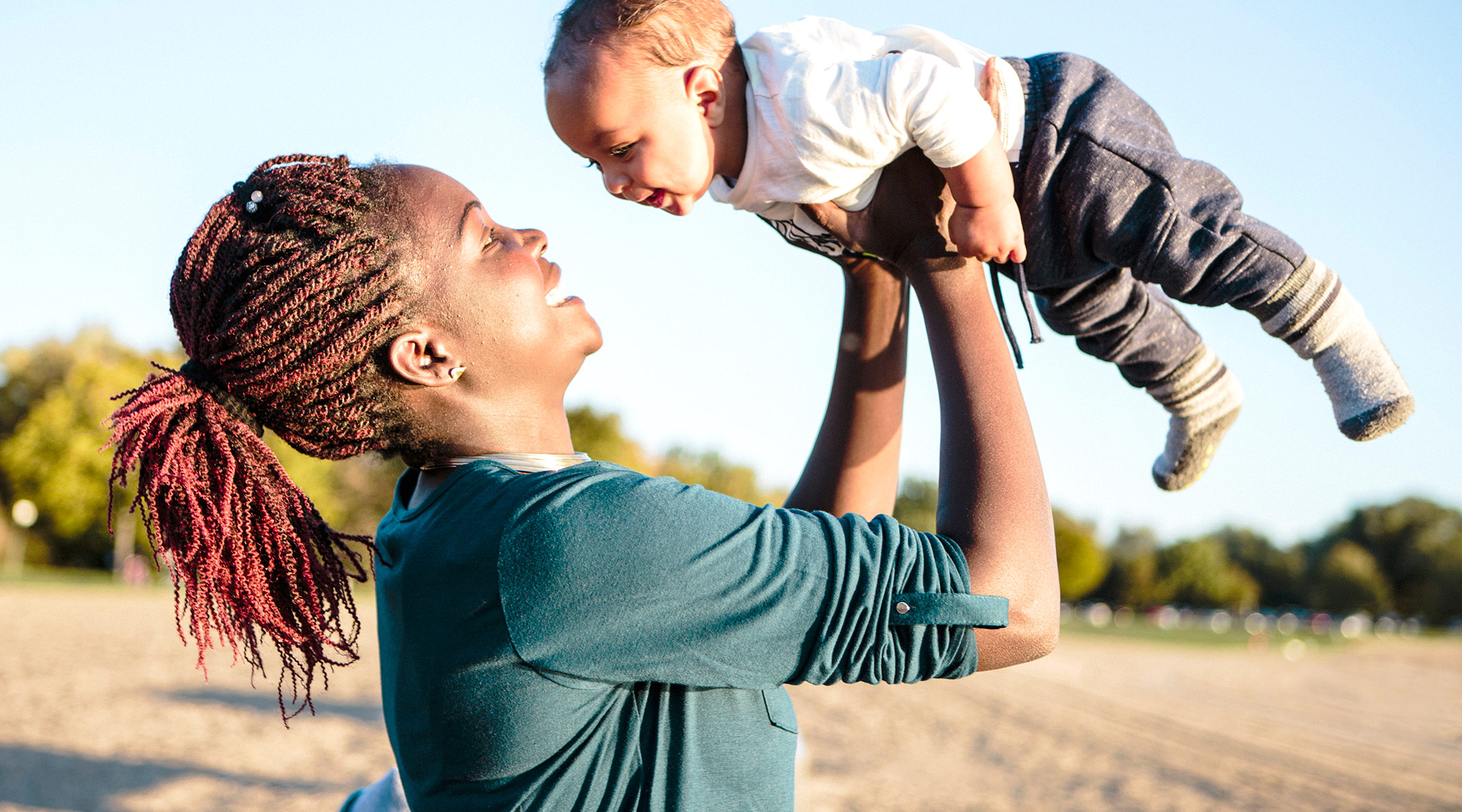 happy mom holds up baby outdoors