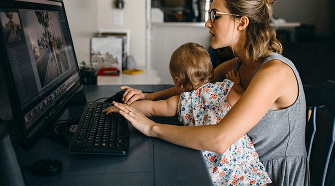 mom struggles to work from home on her computer with baby in her lap