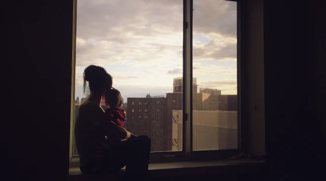 mother and baby sitting on window in new york city apartment looking out the window
