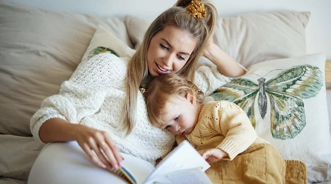 mother and baby reading a book on the couch at home