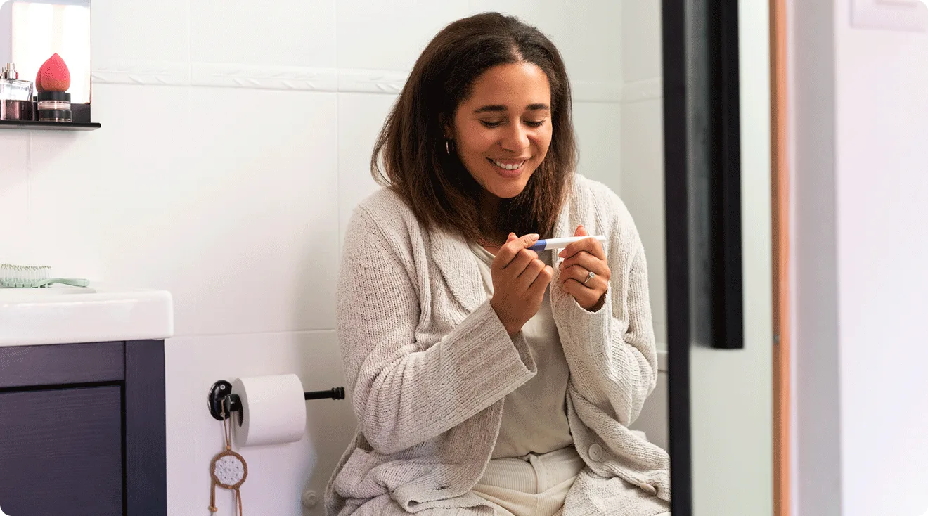 happy woman looking at pregnancy test in bathroom