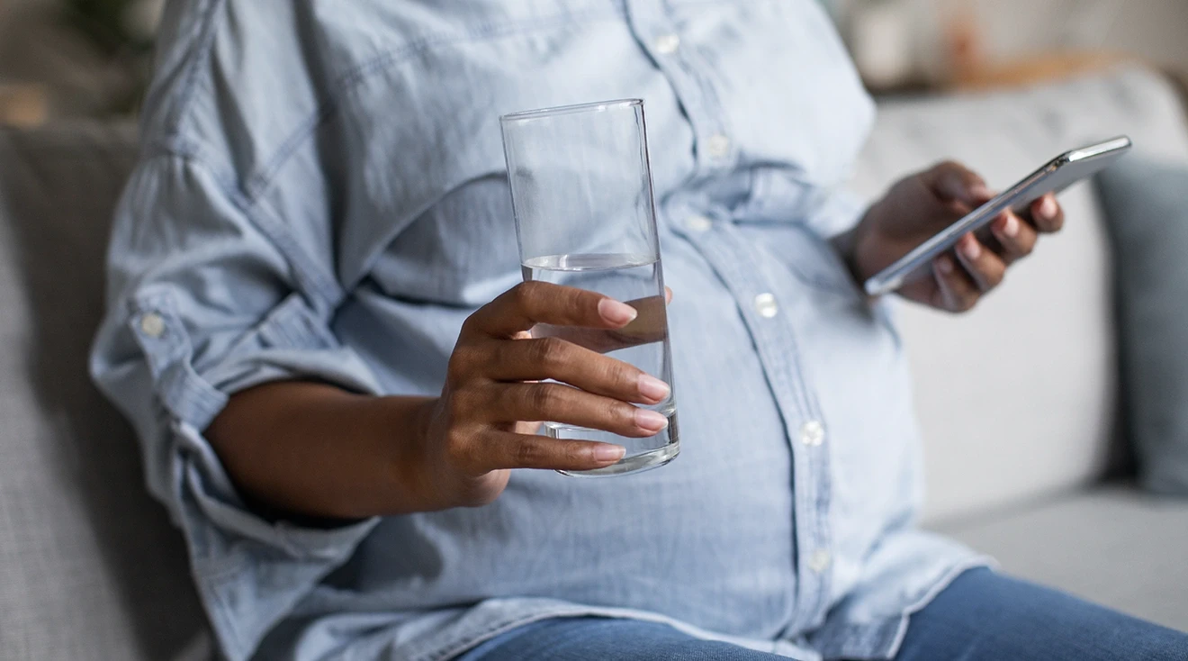 pregnant holding a glass of water while looking at phone
