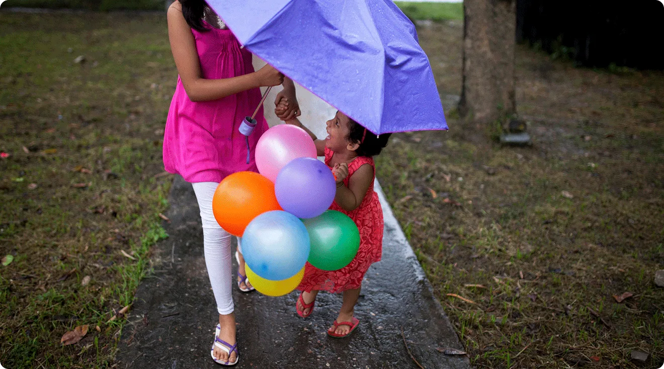 toddler and older sister in the rain holding an umbrella