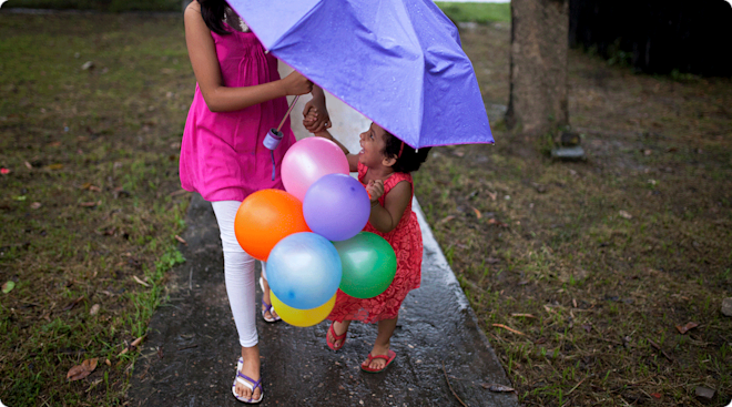 toddler and older sister in the rain holding an umbrella