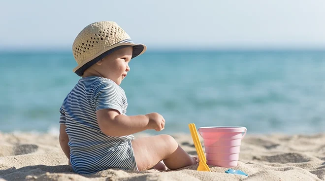 baby wearing a sun hat and sitting on the beach with toys