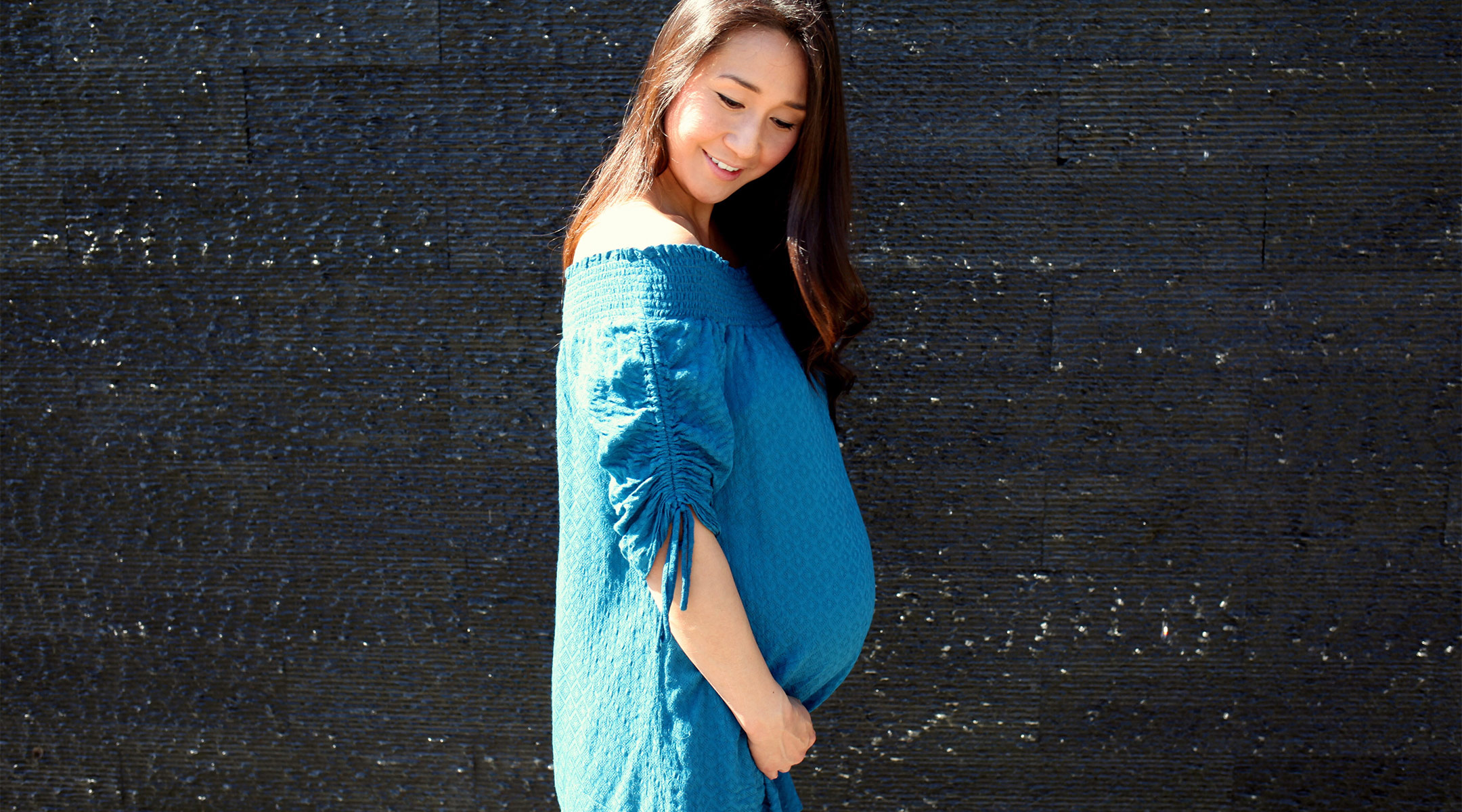 happy pregnant woman standing in the sun against neutral background