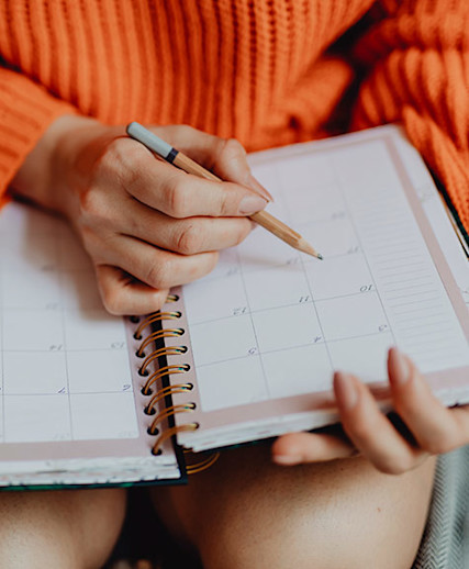 woman in orange sweater making notes in her calendar