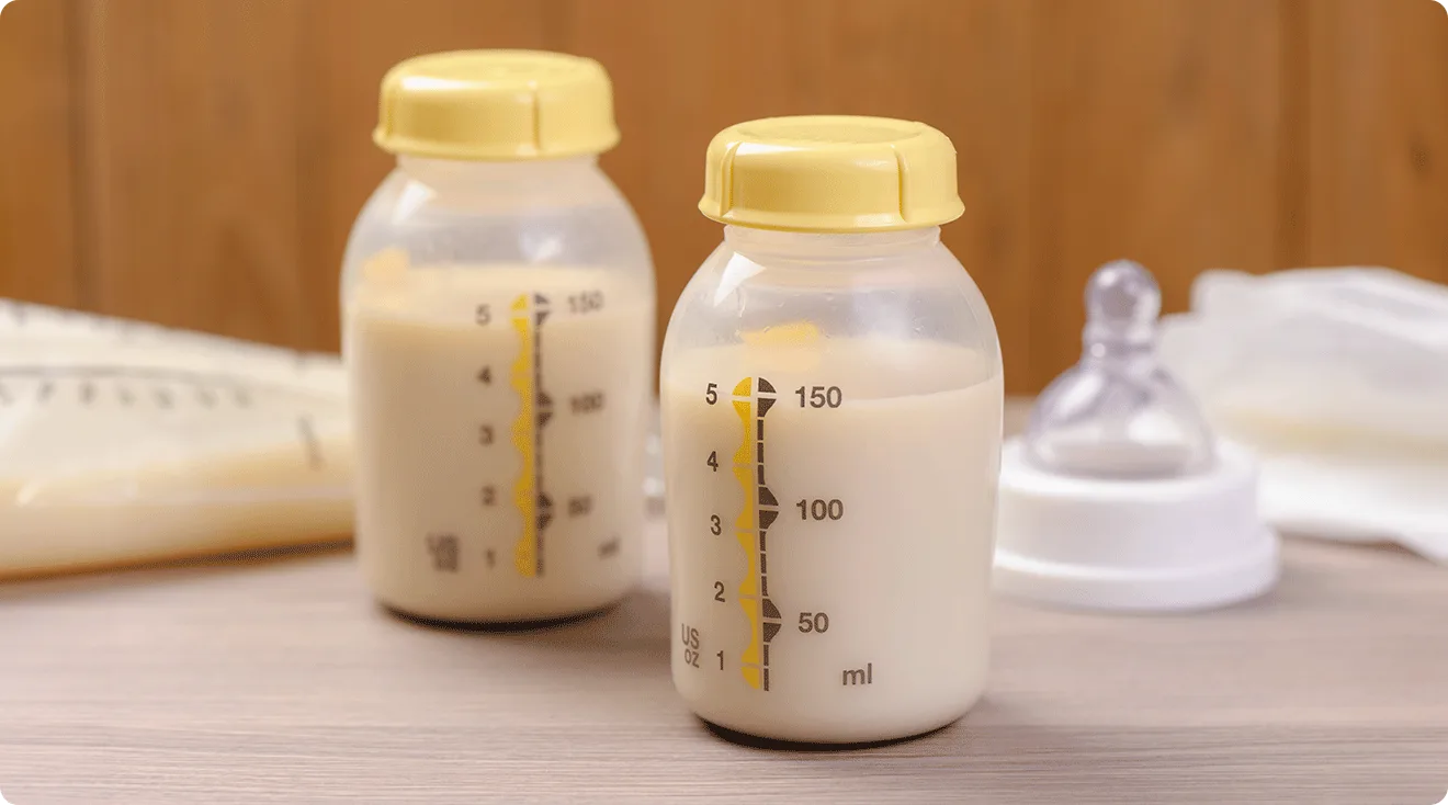 baby bottles filled with milk with bottle nipple and breast milk storage bag in the background