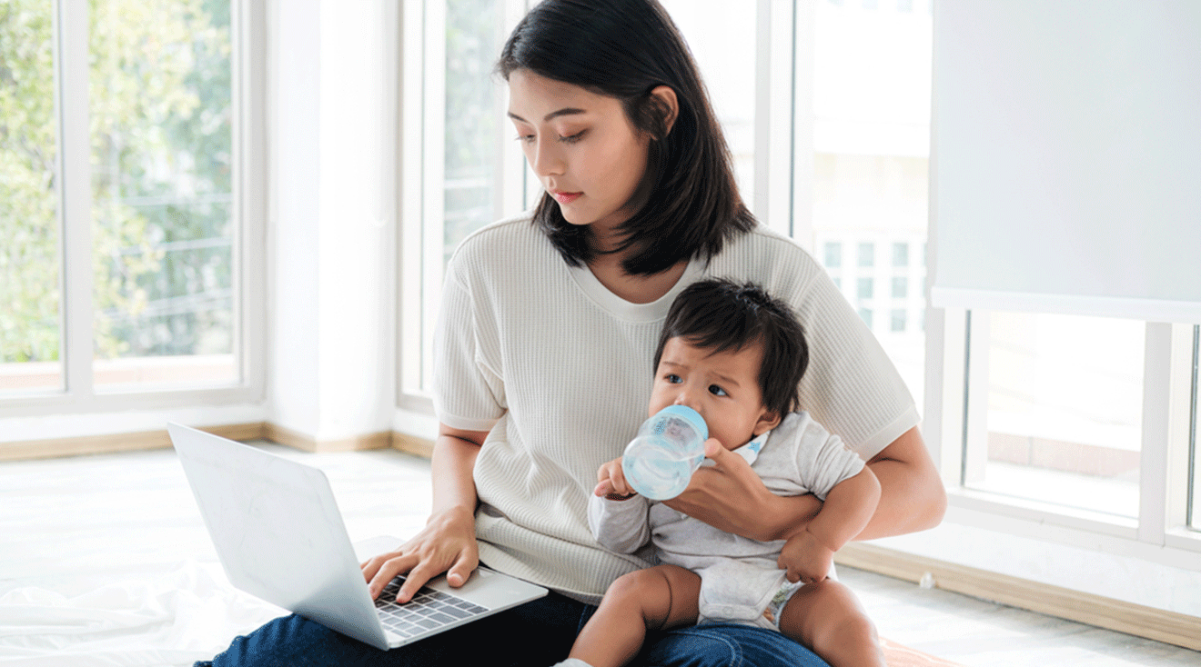 mom holding baby while working on laptop at home