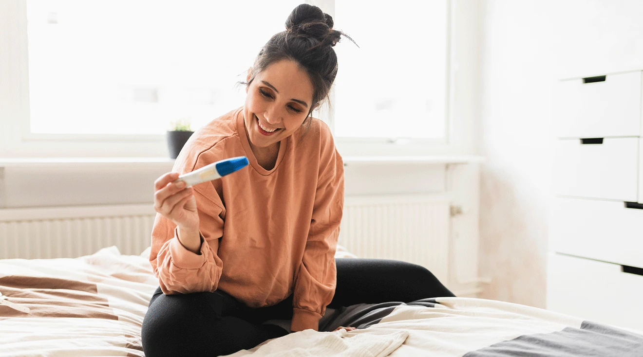 woman smiling while holding pregnancy test at home