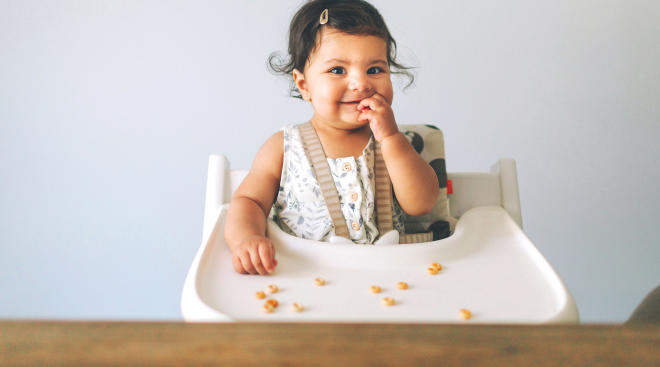 happy baby eating solid foods in high chair