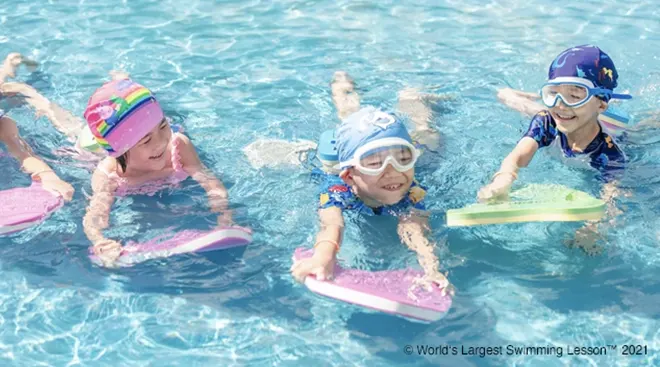 group of children learning how to swim with kick boards in pool