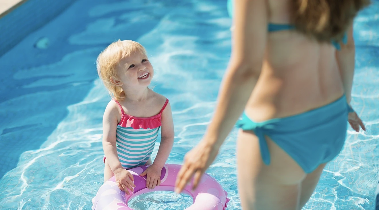 toddler smiling at mom while playing in the pool on a summer day