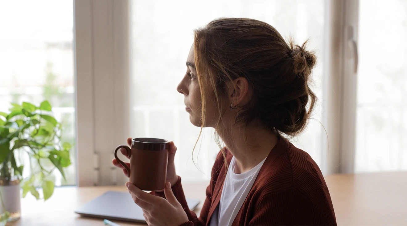 woman sitting at home thinking while holding a coffee mug