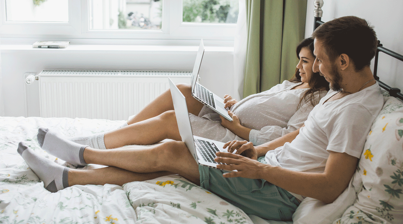 pregnant woman and husband using laptops in bed to start baby registry