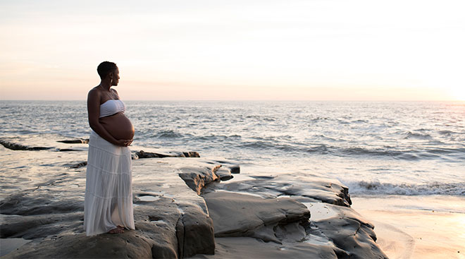 black pregnant woman standing on the beach during sunset