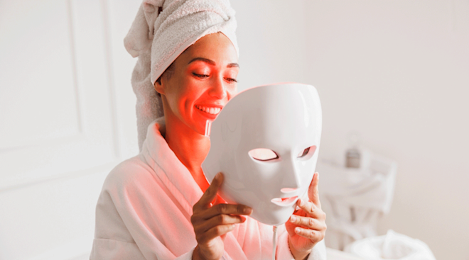 woman putting LED red light face mask on at home