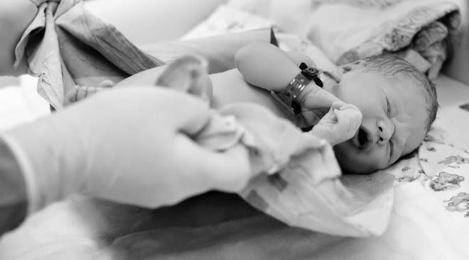 Black and white photo of gloved doctor caring for newborn in the delivery room