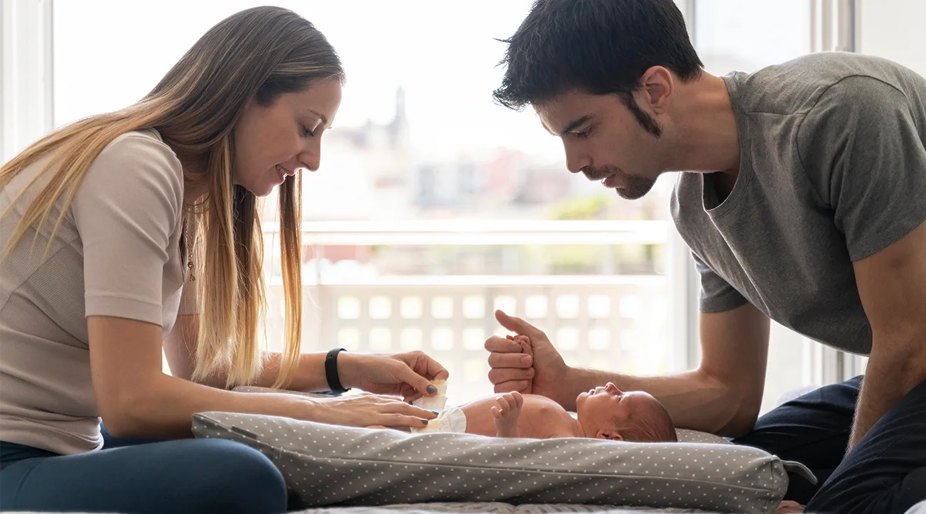 parents changing newborn baby's diaper at home