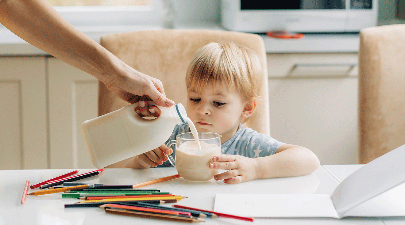 mom pouring cow's milk for toddler into glass at kitchen table