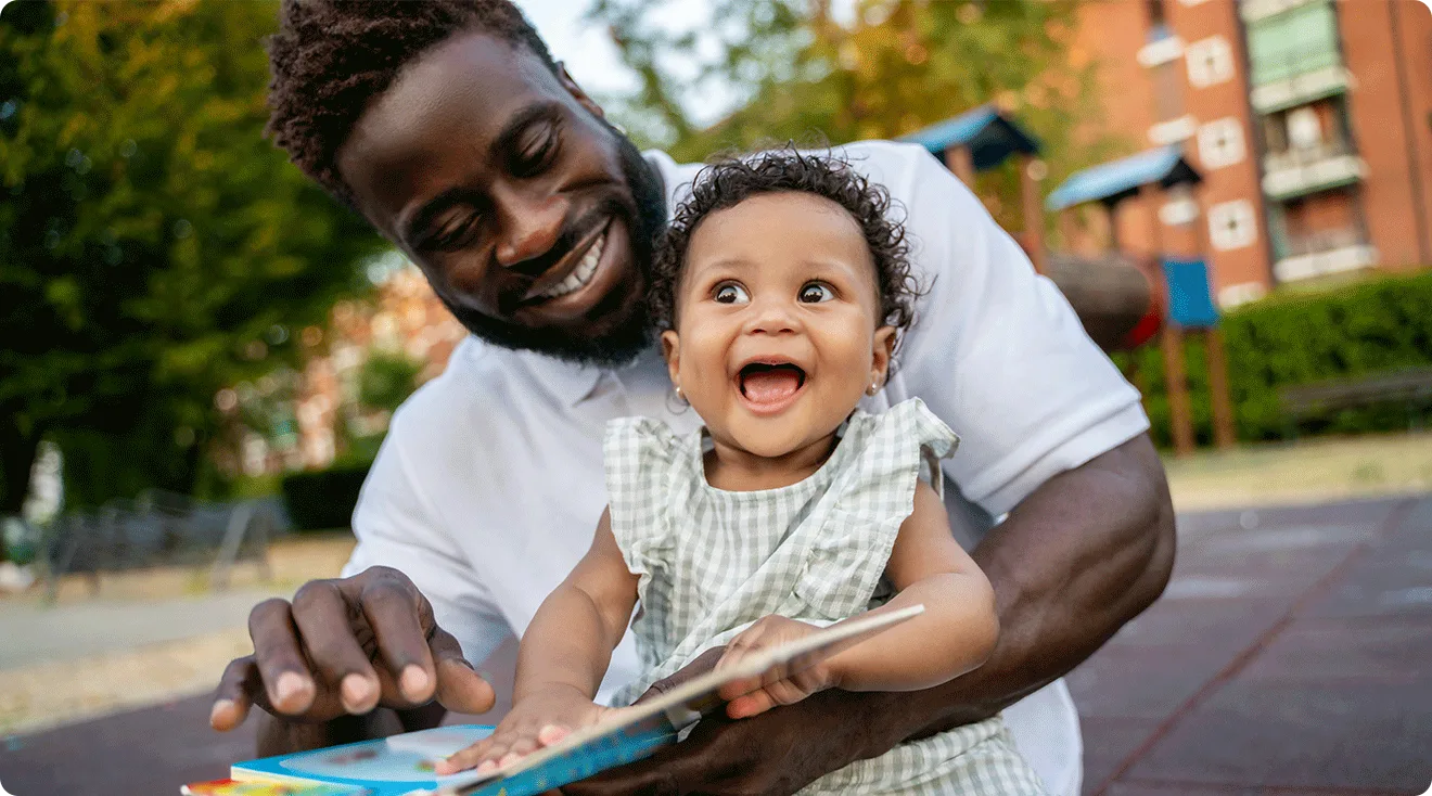 dad laughing with baby while reading a book outside