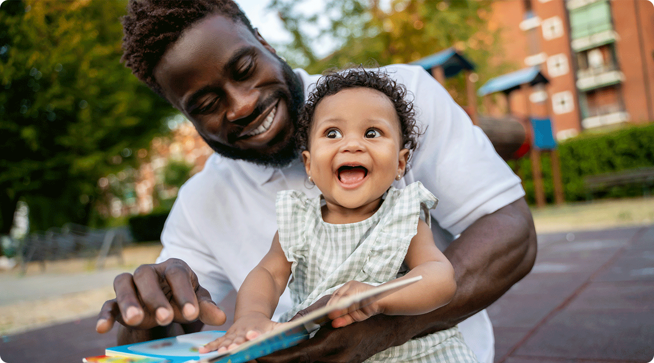 dad laughing with baby while reading a book outside