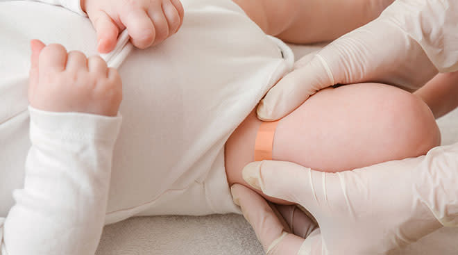 close up of doctor putting band aid on baby's leg after flu shot