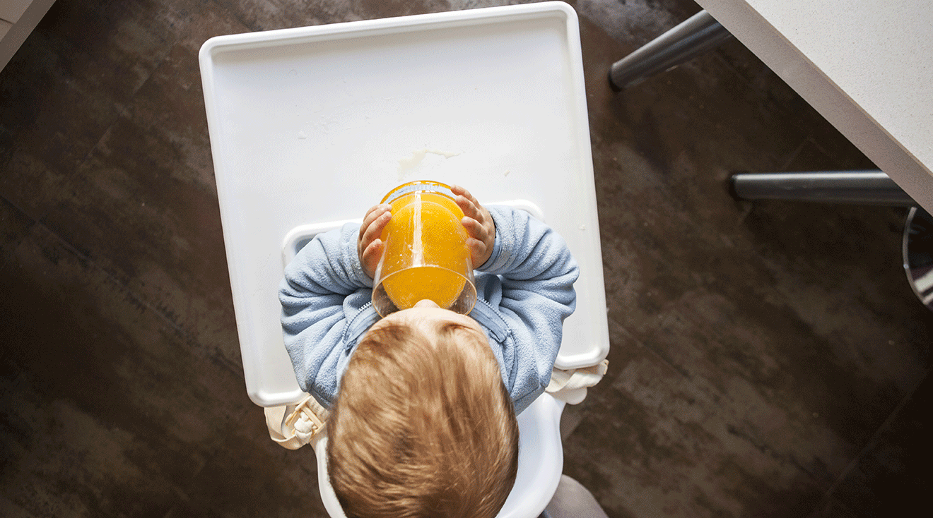 baby drinking orange juice in high chair