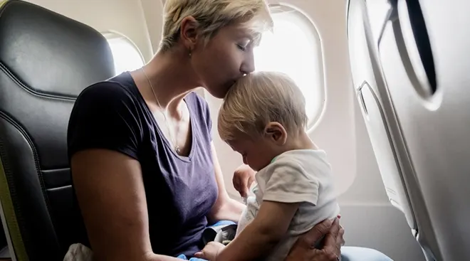 mother kissing baby's head while sitting on airplane
