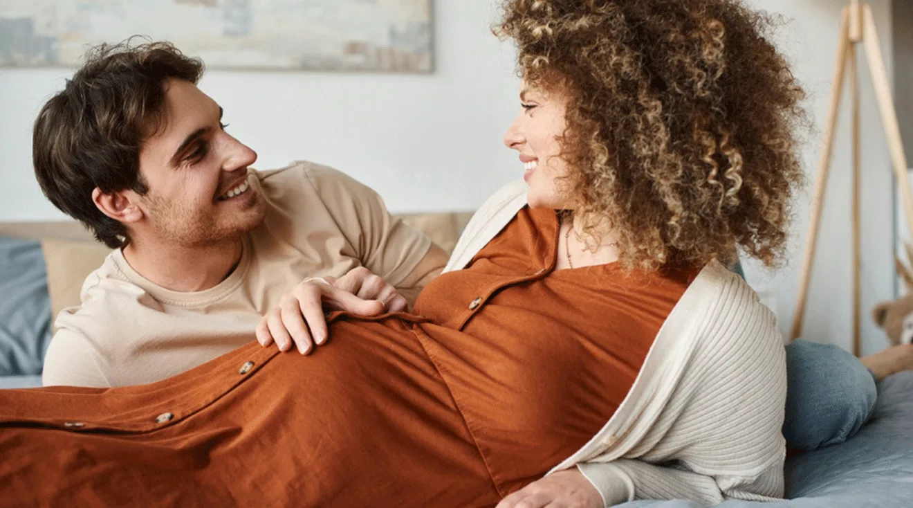 pregnant couple looking at each other in bed
