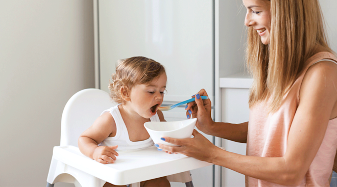 mom feeding 1 year old in high chair